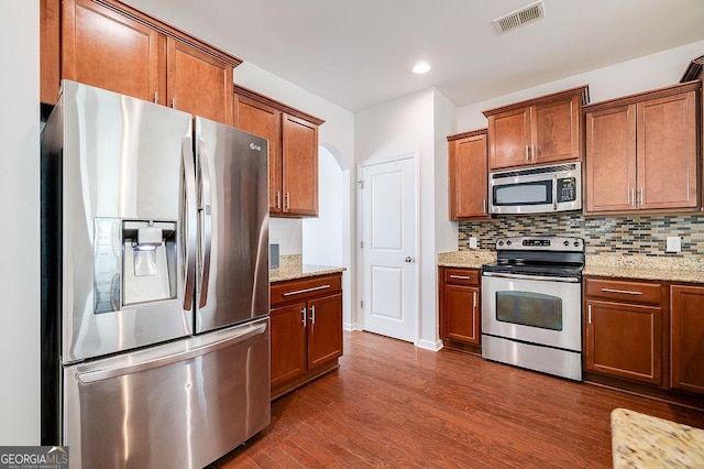 kitchen featuring stainless steel appliances, dark wood-style floors, backsplash, brown cabinets, and recessed lighting