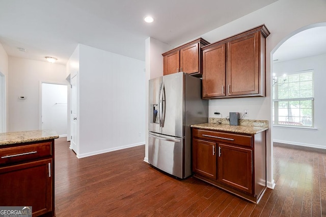 kitchen featuring stainless steel refrigerator with ice dispenser, arched walkways, dark wood finished floors, light stone counters, and recessed lighting