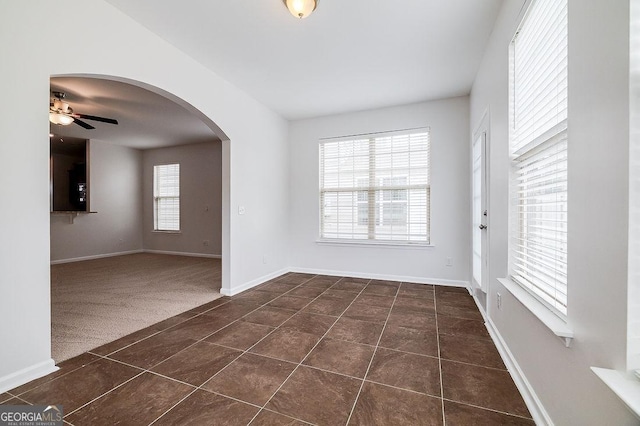 empty room featuring ceiling fan, dark tile patterned flooring, baseboards, arched walkways, and dark carpet