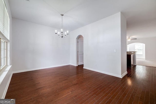 spare room with arched walkways, a chandelier, dark wood-style floors, baseboards, and ceiling fan