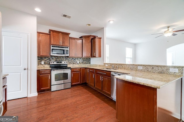 kitchen with stainless steel appliances, a sink, dark wood-style floors, brown cabinets, and a peninsula