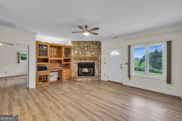 unfurnished living room with a ceiling fan, crown molding, plenty of natural light, a stone fireplace, and light wood-style floors