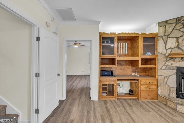 unfurnished living room featuring ornamental molding, light wood-type flooring, a ceiling fan, a wood stove, and stairway