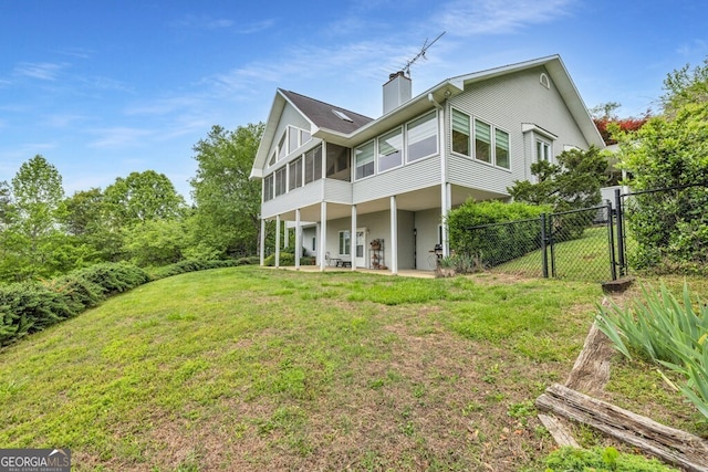 back of house featuring a sunroom, a gate, a chimney, and a patio