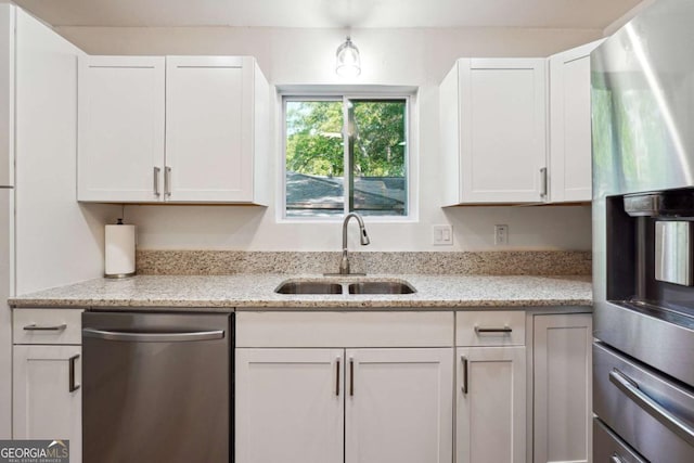 kitchen with stainless steel appliances, a sink, white cabinetry, and light stone countertops