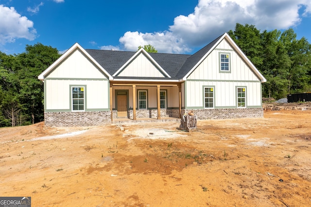modern inspired farmhouse featuring covered porch, brick siding, board and batten siding, and a shingled roof