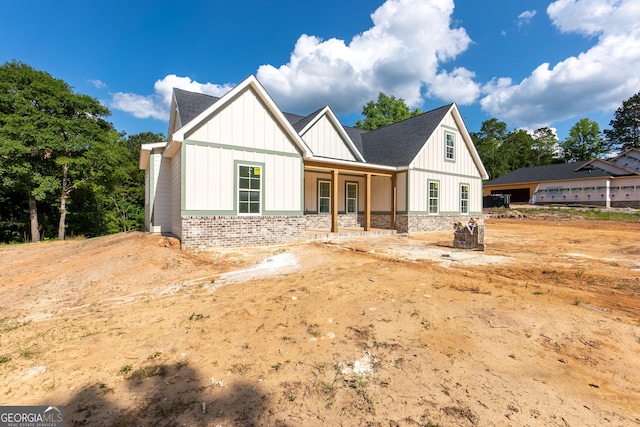 modern farmhouse featuring board and batten siding, a shingled roof, and brick siding