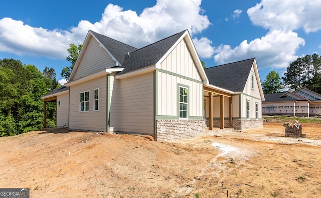 view of property exterior with board and batten siding, brick siding, and a shingled roof