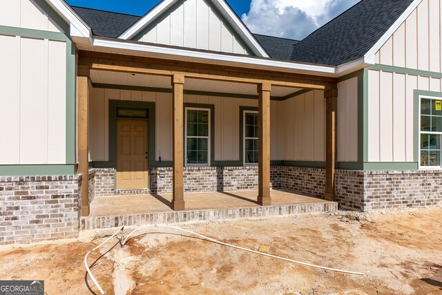 property entrance featuring a shingled roof, board and batten siding, brick siding, and a porch