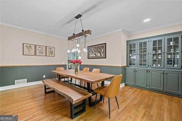 dining area with light wood-style floors, a wainscoted wall, and crown molding