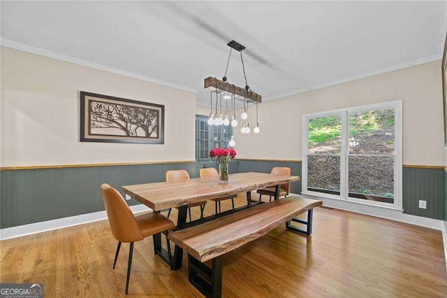dining space featuring a wainscoted wall, wood finished floors, ornamental molding, and a chandelier