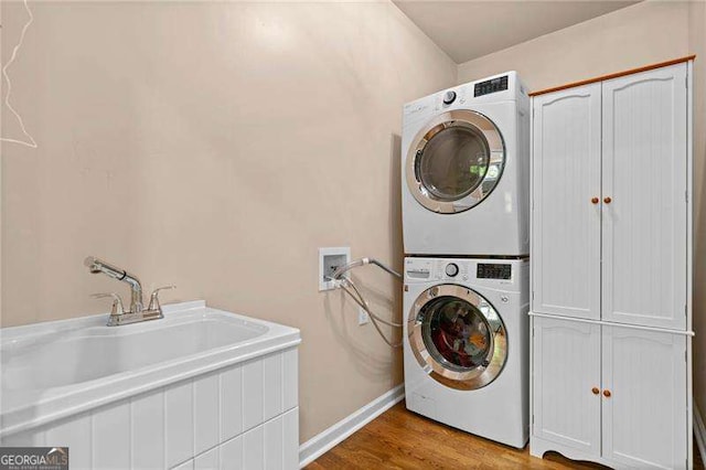 washroom with stacked washer / dryer, cabinet space, light wood finished floors, and baseboards