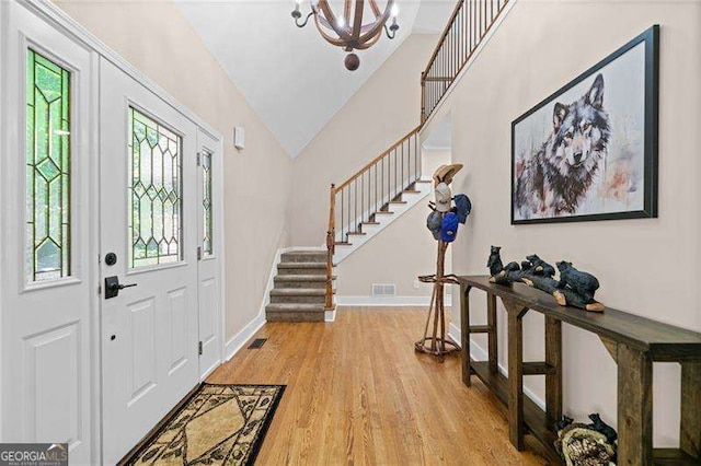 foyer entrance featuring stairway, light wood-style flooring, a chandelier, vaulted ceiling, and baseboards