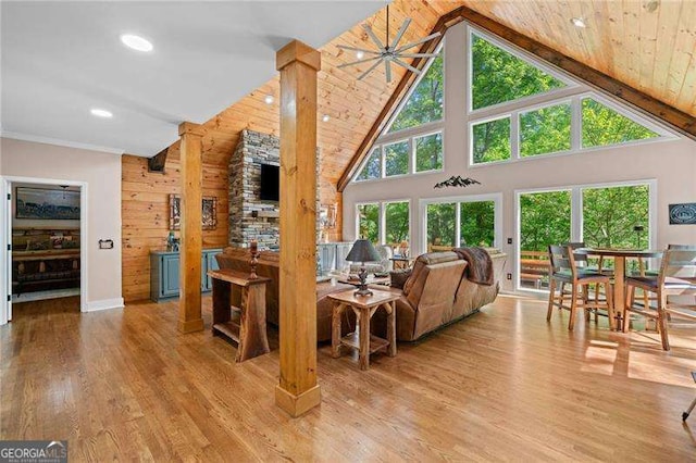 living room featuring plenty of natural light, high vaulted ceiling, light wood finished floors, recessed lighting, and wooden walls