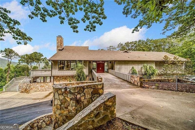 single story home featuring a chimney, concrete driveway, stairs, and fence