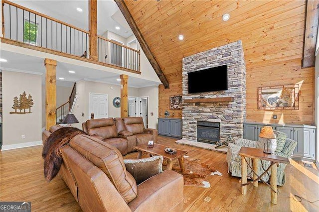 living area featuring high vaulted ceiling, ornate columns, light wood finished floors, a stone fireplace, and recessed lighting