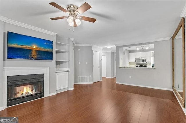 unfurnished living room with ceiling fan, wood finished floors, ornamental molding, a warm lit fireplace, and baseboards