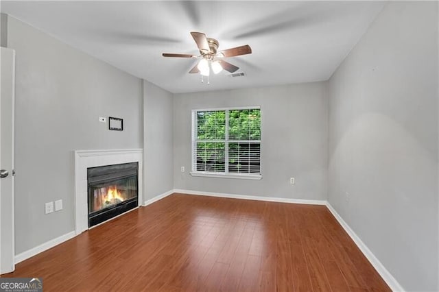 unfurnished living room with a ceiling fan, a glass covered fireplace, wood finished floors, and baseboards