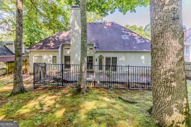 rear view of property featuring stucco siding, fence, a chimney, and a shingled roof