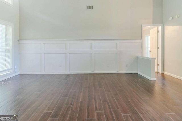 spare room featuring a decorative wall, dark wood-style floors, and wainscoting