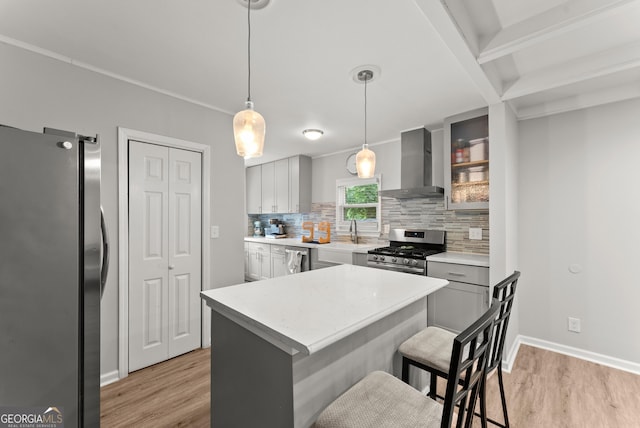 kitchen featuring appliances with stainless steel finishes, wall chimney exhaust hood, light wood finished floors, and backsplash