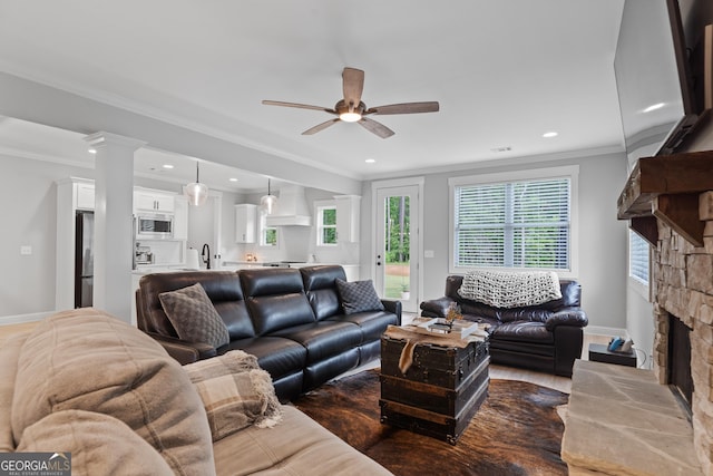 living room featuring a stone fireplace, ceiling fan, ornamental molding, recessed lighting, and baseboards