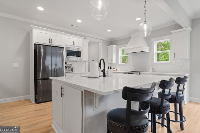 kitchen with appliances with stainless steel finishes, white cabinetry, premium range hood, decorative backsplash, and an island with sink