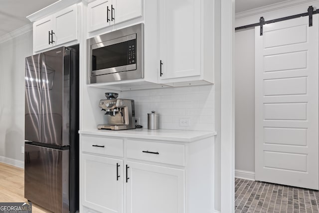 kitchen featuring stainless steel appliances, baseboards, crown molding, tasteful backsplash, and a barn door