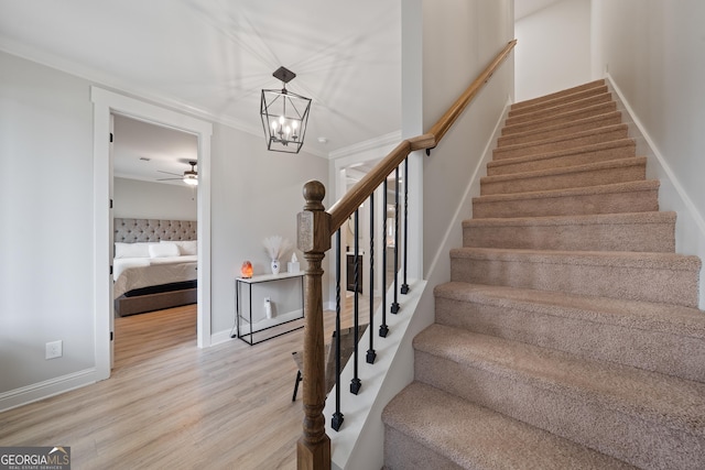 stairway featuring wood finished floors, a chandelier, ceiling fan, baseboards, and ornamental molding