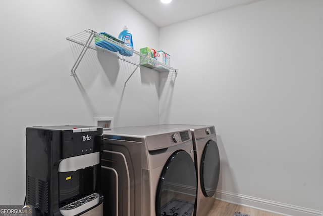 clothes washing area featuring washing machine and clothes dryer, wood finished floors, and baseboards