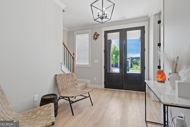 entryway featuring french doors, crown molding, light wood-style flooring, a chandelier, and stairs