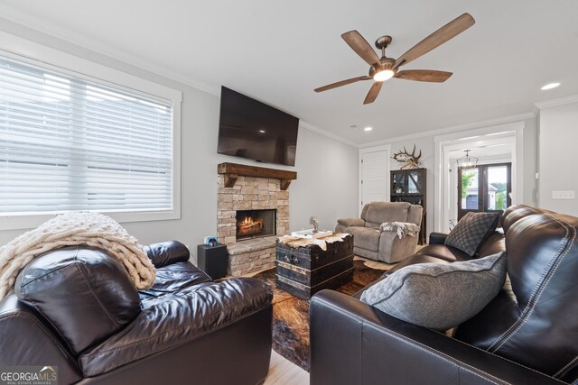 living area featuring wood finished floors, ceiling fan, ornamental molding, recessed lighting, and a stone fireplace