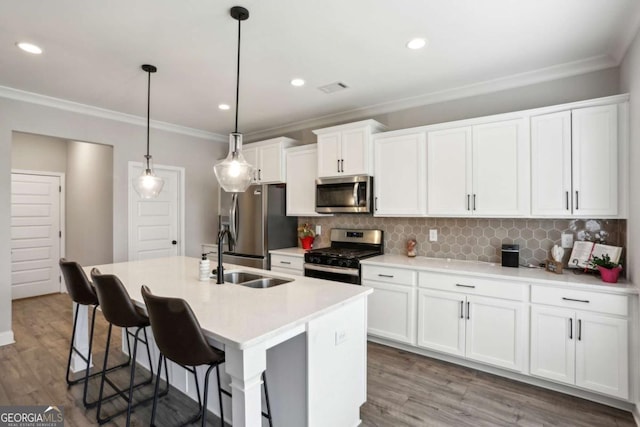 kitchen with appliances with stainless steel finishes, a sink, ornamental molding, an island with sink, and white cabinetry