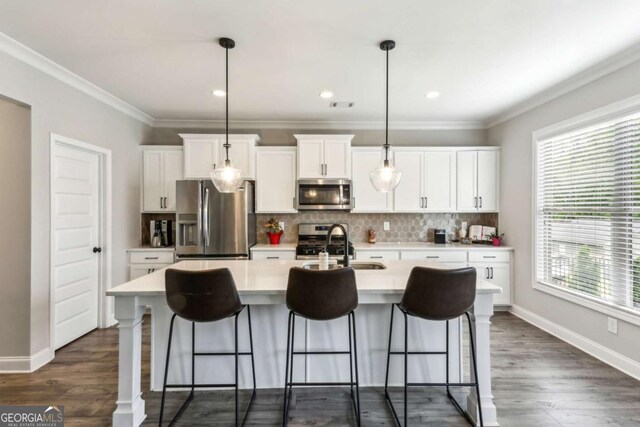 kitchen featuring appliances with stainless steel finishes, tasteful backsplash, light countertops, a center island with sink, and a breakfast bar area