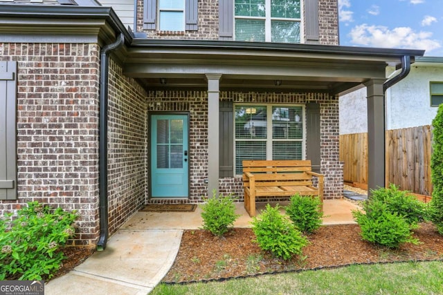 view of exterior entry with brick siding, fence, and a porch