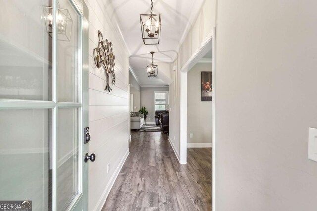 corridor featuring a chandelier, ornamental molding, wood finished floors, and baseboards