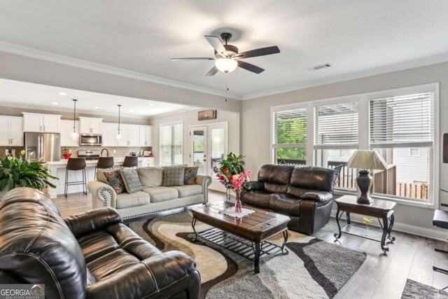 living area with healthy amount of natural light, a ceiling fan, light wood-style flooring, ornamental molding, and baseboards