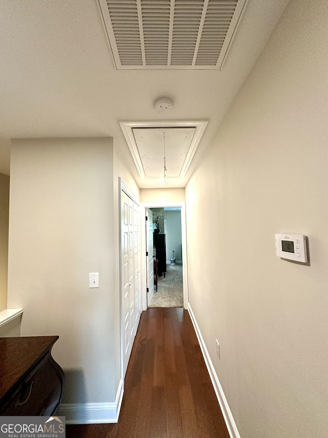 corridor featuring attic access, baseboards, and dark wood finished floors