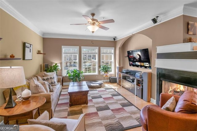 living room with ornamental molding, ceiling fan, and a lit fireplace