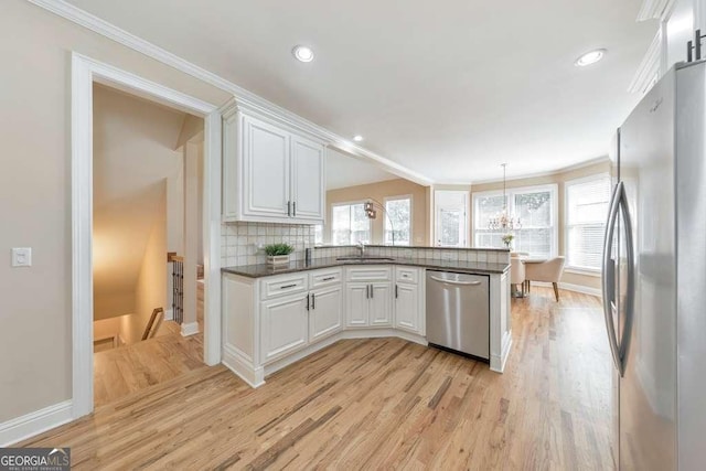 kitchen with appliances with stainless steel finishes, a sink, light wood-type flooring, a peninsula, and ornamental molding