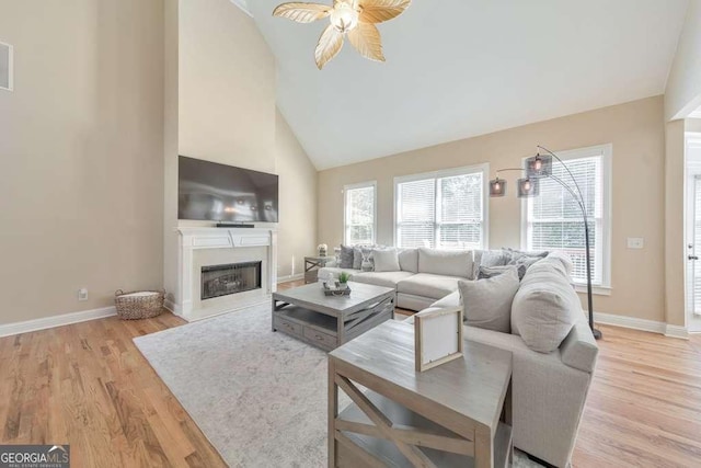living area with a ceiling fan, light wood finished floors, healthy amount of natural light, and high vaulted ceiling