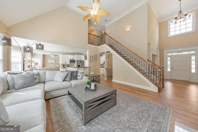 living room featuring ceiling fan, a high ceiling, stairs, a chandelier, and crown molding