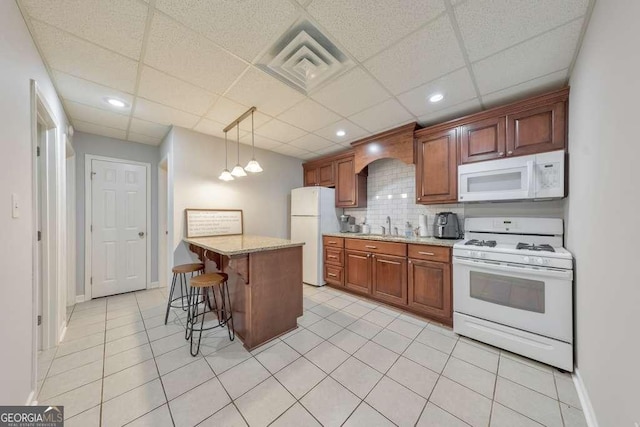 kitchen with white appliances, a sink, a kitchen breakfast bar, a drop ceiling, and light tile patterned flooring