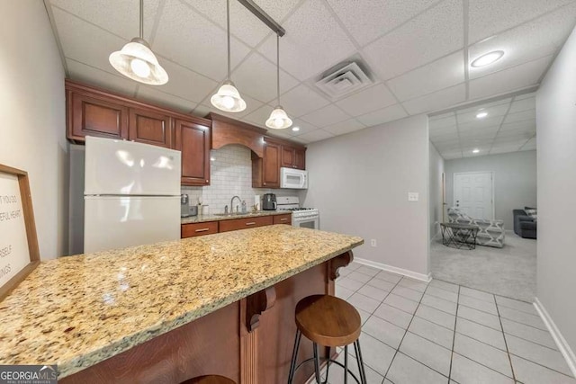 kitchen with white appliances, a sink, light tile patterned floors, baseboards, and a breakfast bar area