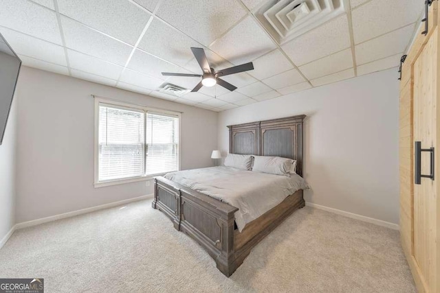 bedroom with a drop ceiling, light carpet, a barn door, and baseboards