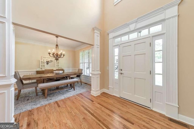 entryway with light wood finished floors, a chandelier, ornamental molding, and a high ceiling
