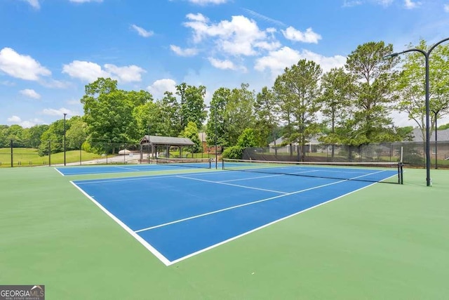 view of tennis court featuring fence, community basketball court, and view of wooded area
