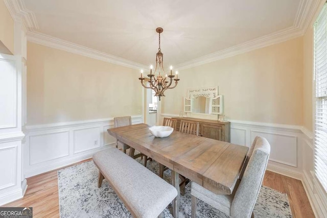 dining space featuring a chandelier, healthy amount of natural light, light wood-style flooring, crown molding, and wainscoting