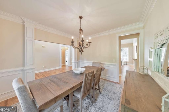 dining area featuring a chandelier, crown molding, light wood-type flooring, a wainscoted wall, and a decorative wall