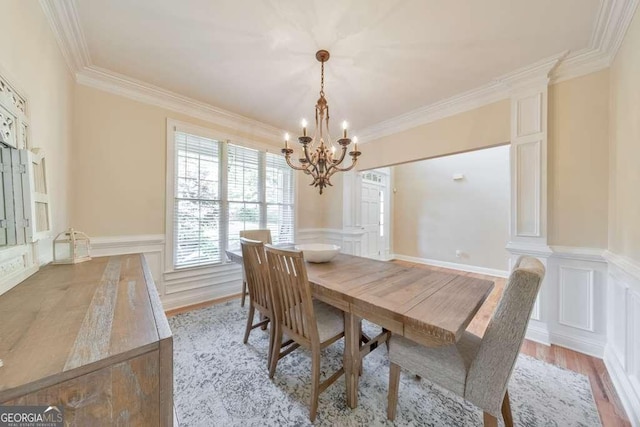 dining space with a chandelier, crown molding, a decorative wall, light wood finished floors, and wainscoting